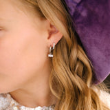 Close-up of a person wearing a small earring with a purple velvet background