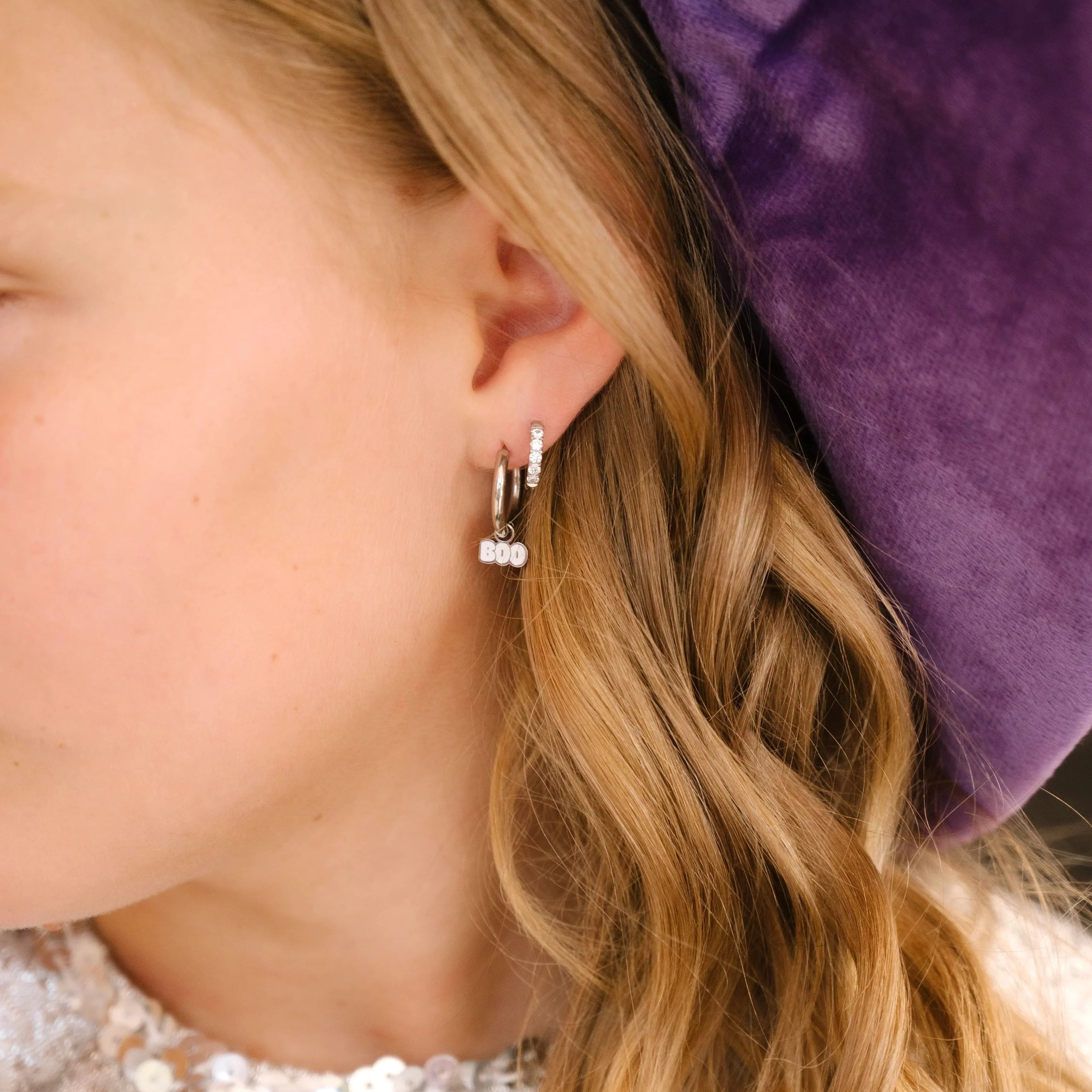 Close-up of a person wearing a small earring with a purple velvet background