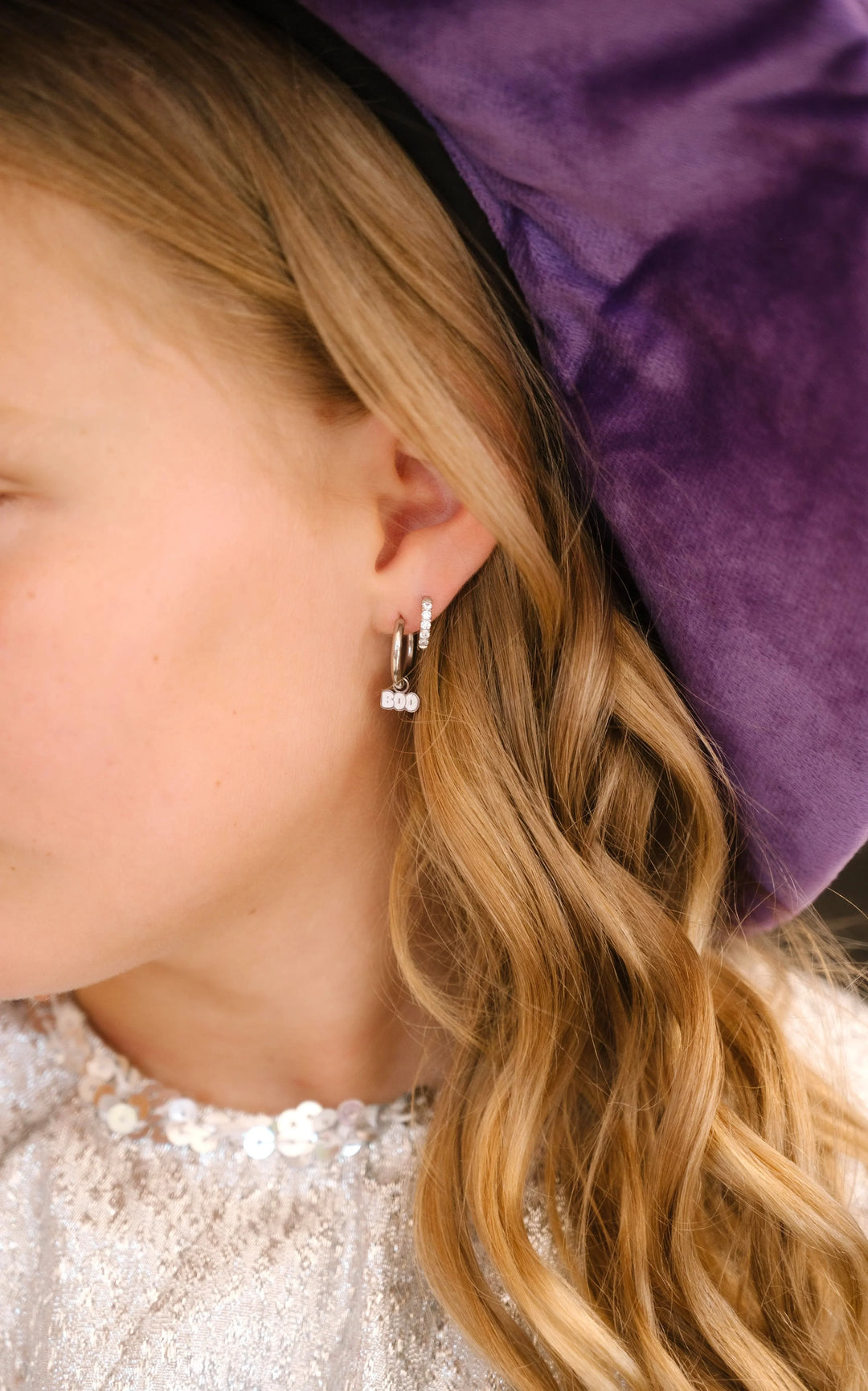 Close-up of a person wearing a small earring with a purple velvet background