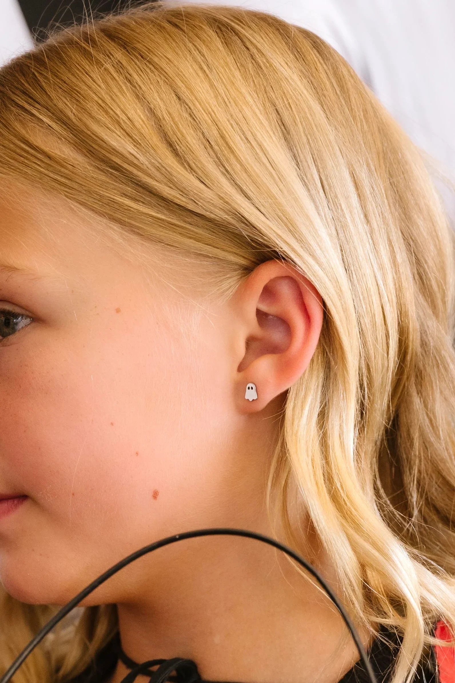 Close-up of a young girl with blonde hair wearing a small ghost-shaped white stud earring.