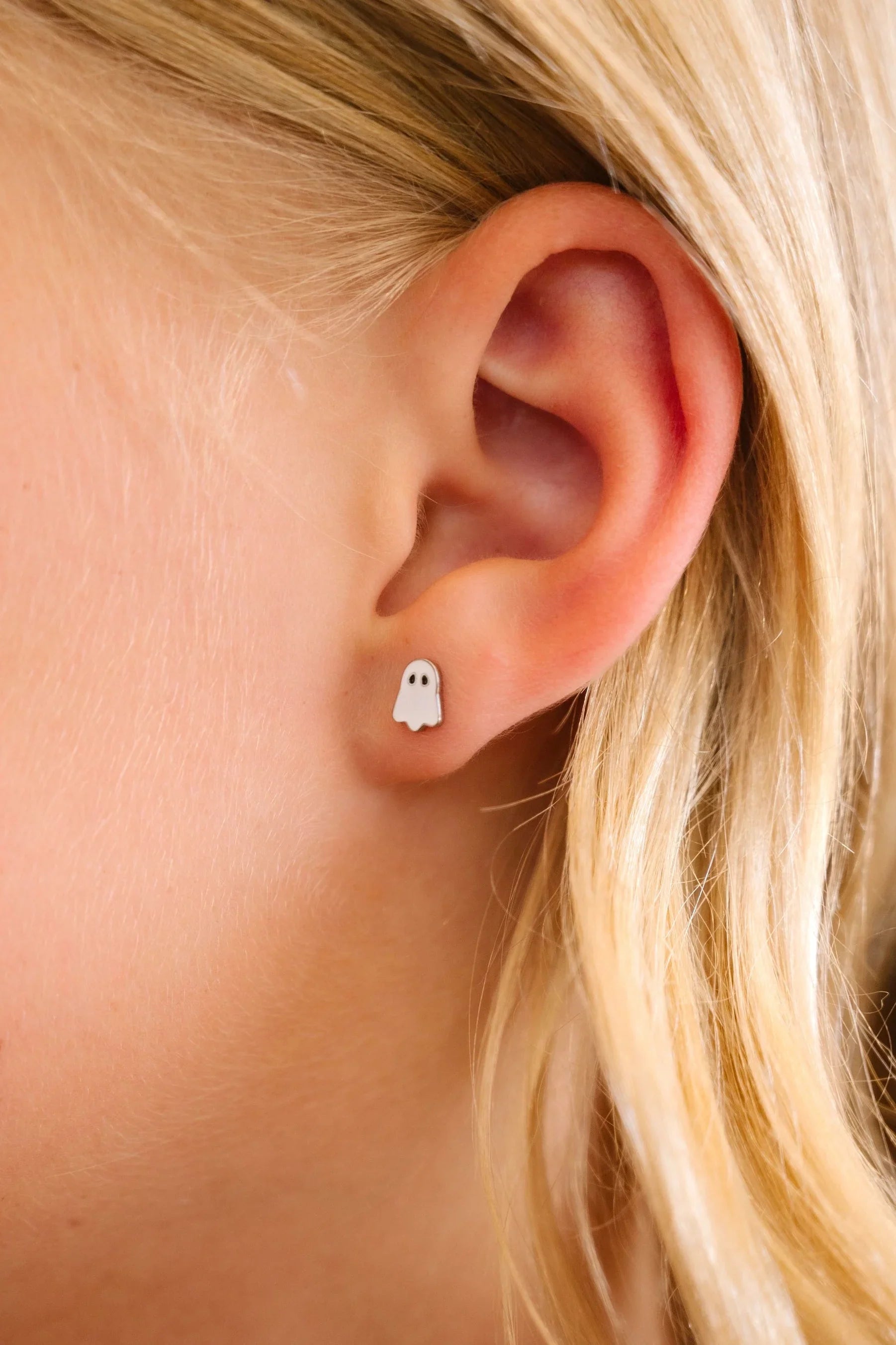 Close-up of an ear wearing a ghost-shaped earring with blonde hair.