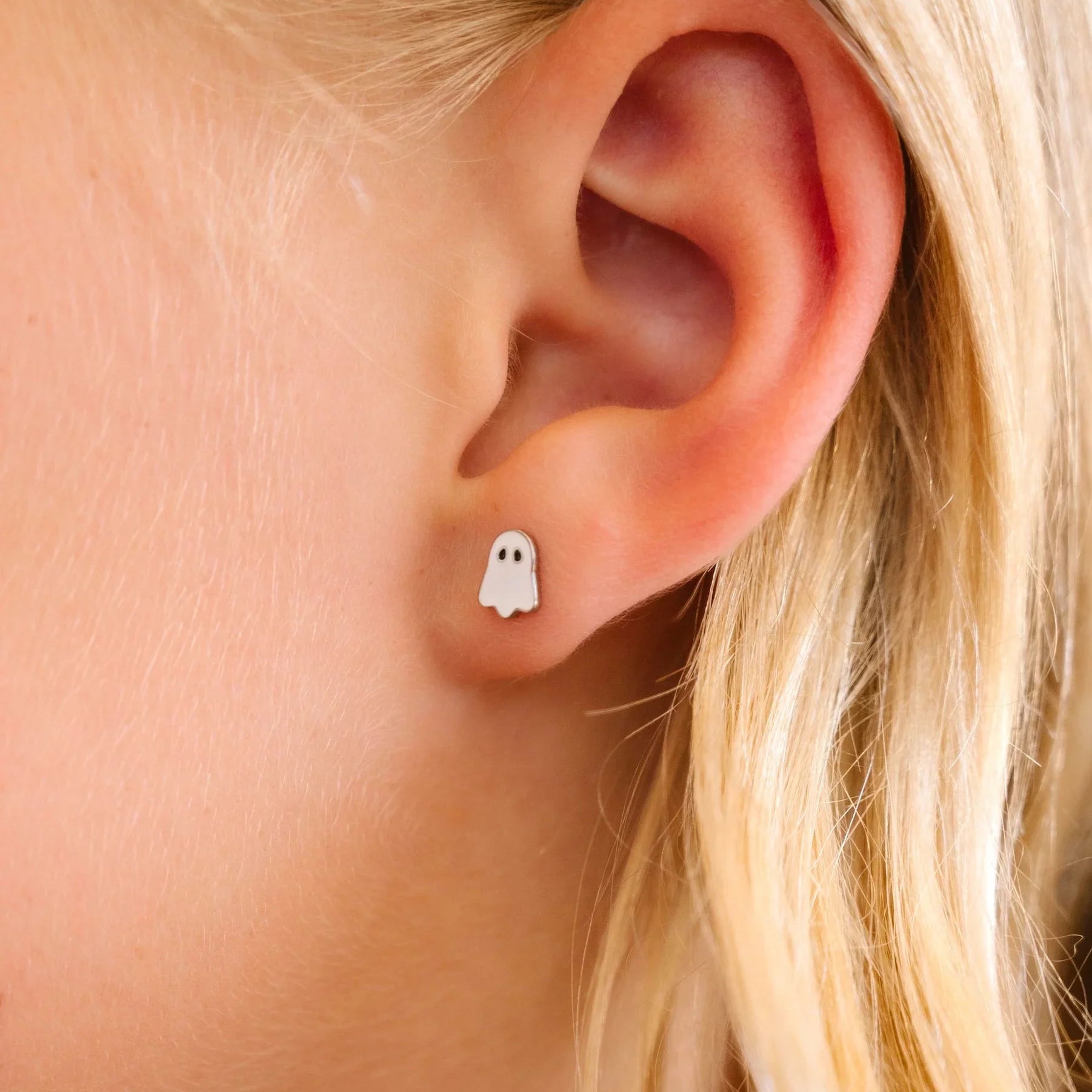 Close-up of an ear wearing a ghost-shaped earring with blonde hair.