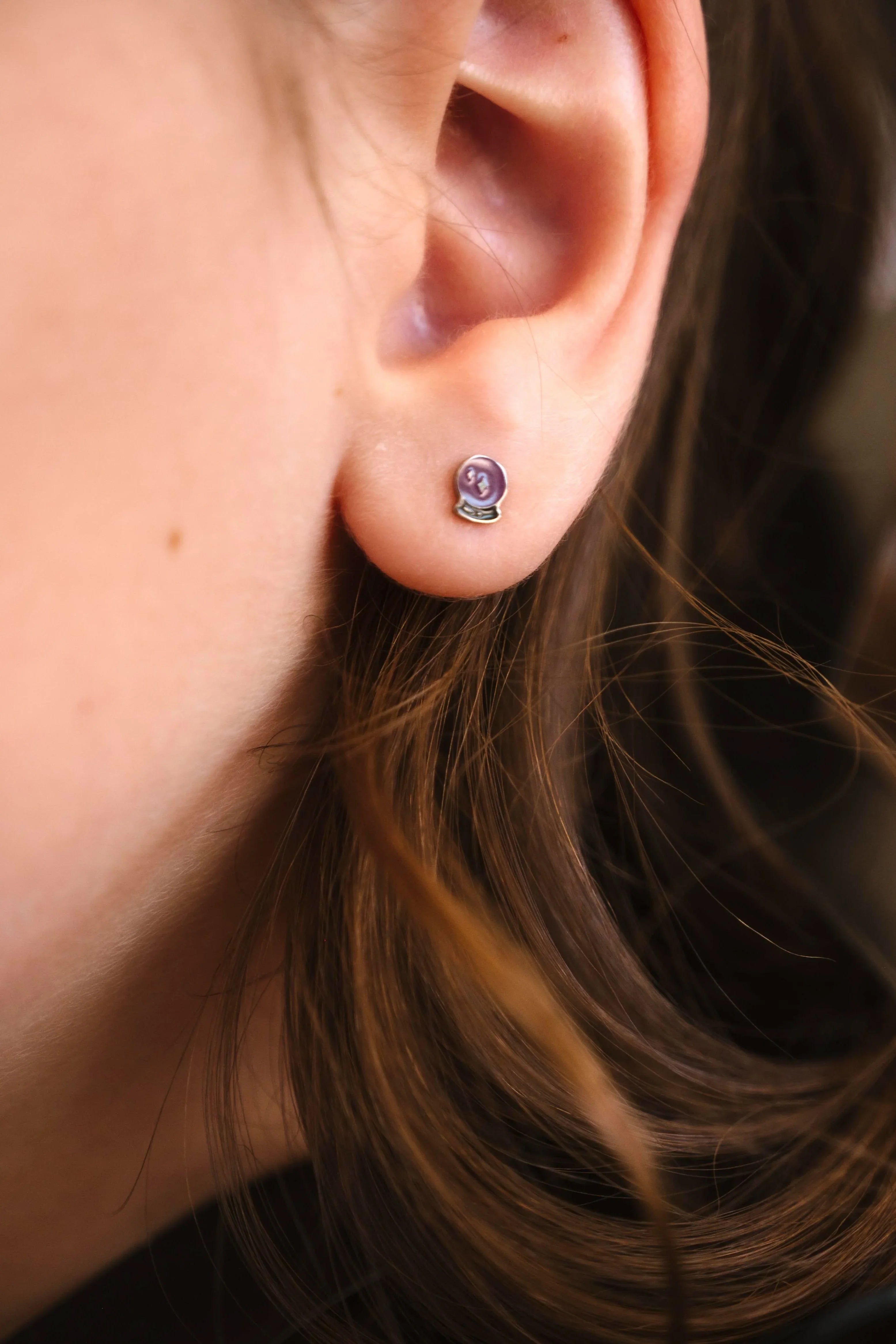 Close-up of an ear wearing a purple crystal ball-shaped earring.