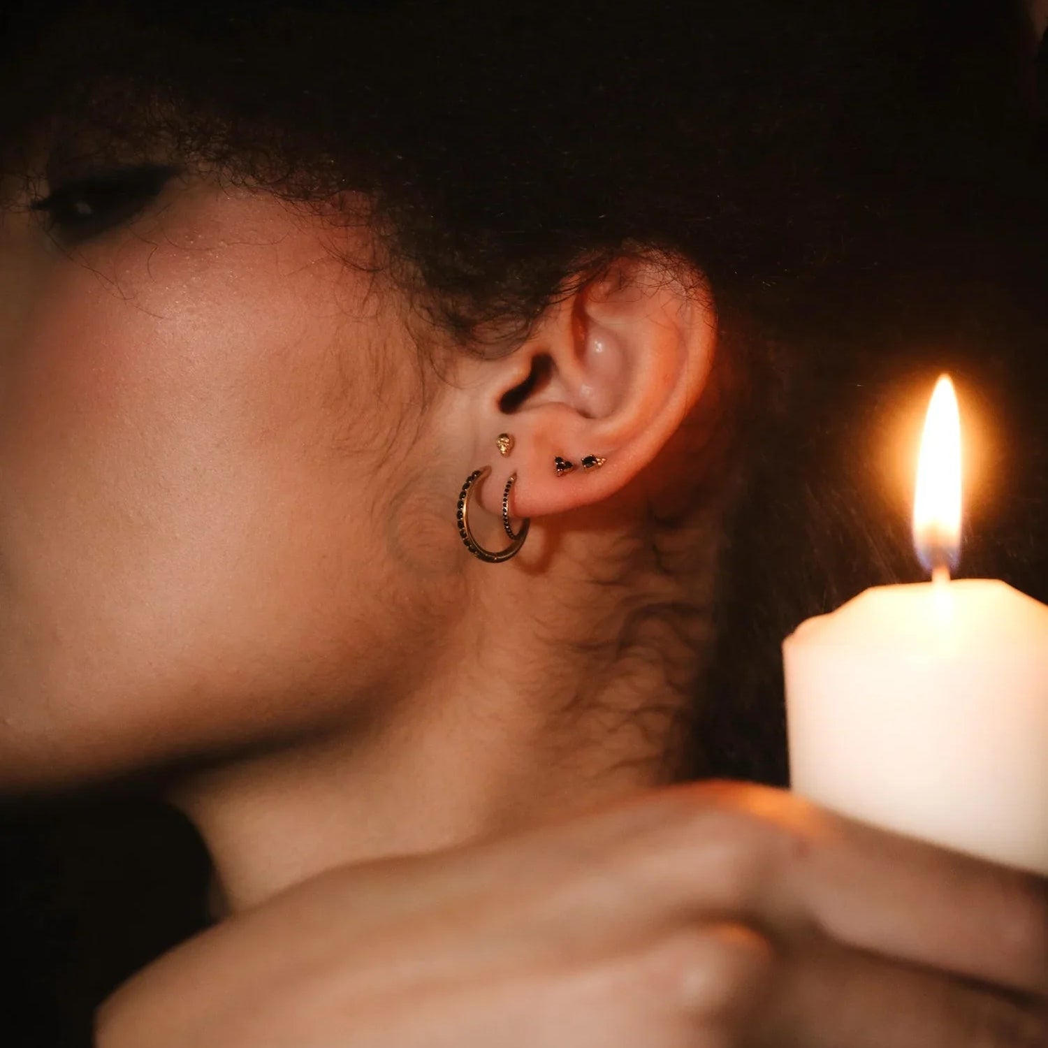 Close up photo of an ear wearing gold and black flat backs and hoops