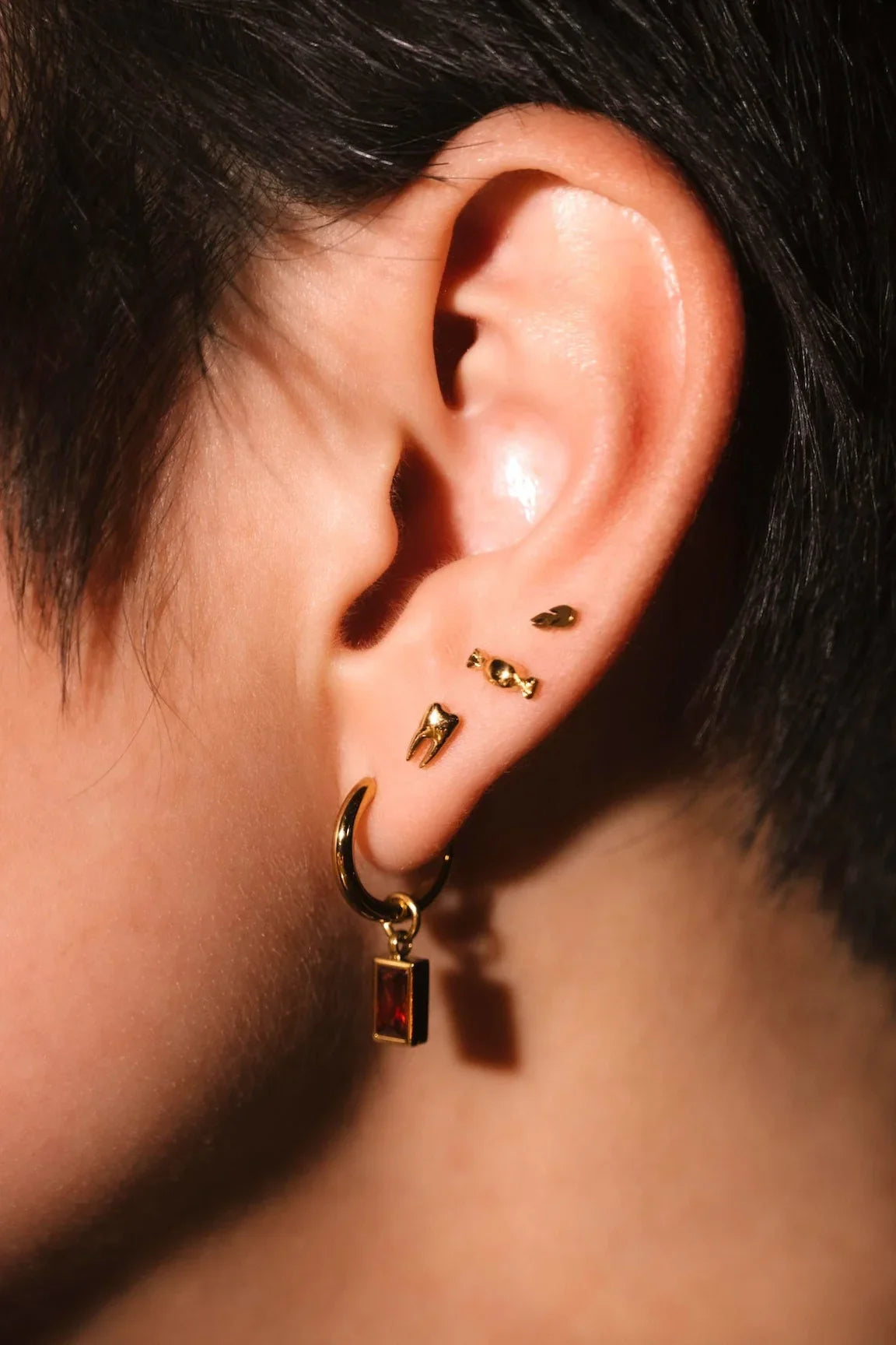 Close up photo of an ear wearing red and gold hoops and flat backs