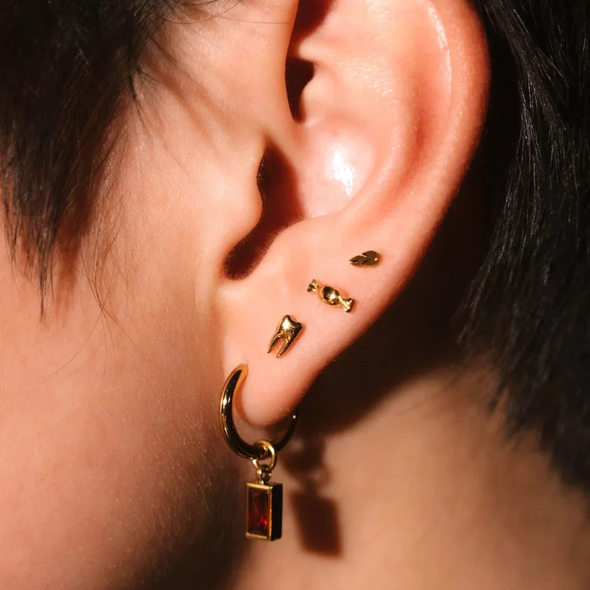 Close up photo of an ear wearing red and gold hoops and flat backs