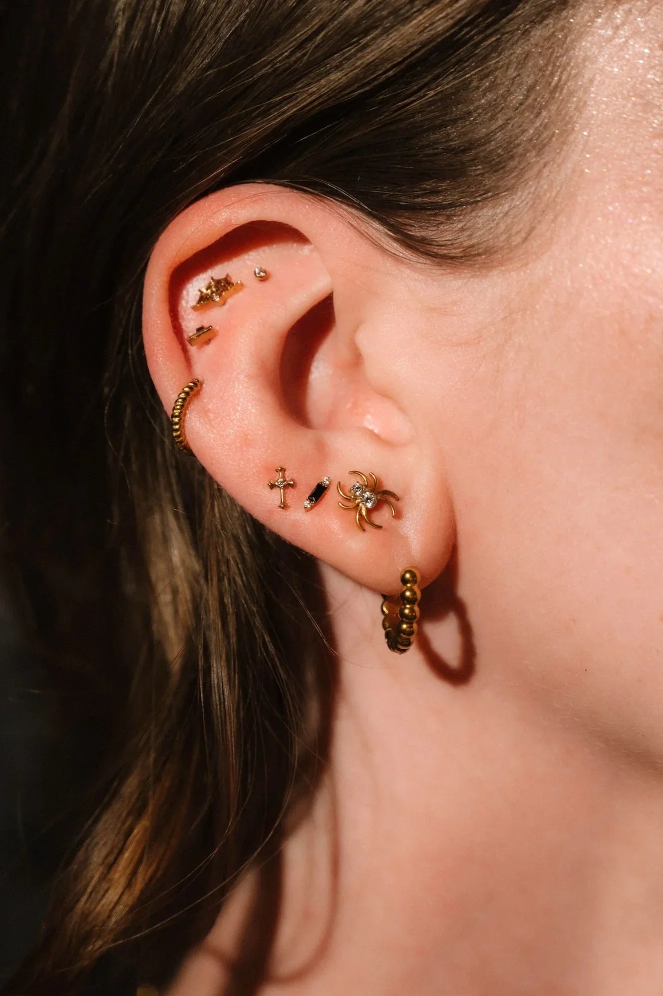 Close up of an ear with black and gold flat backs and hoops