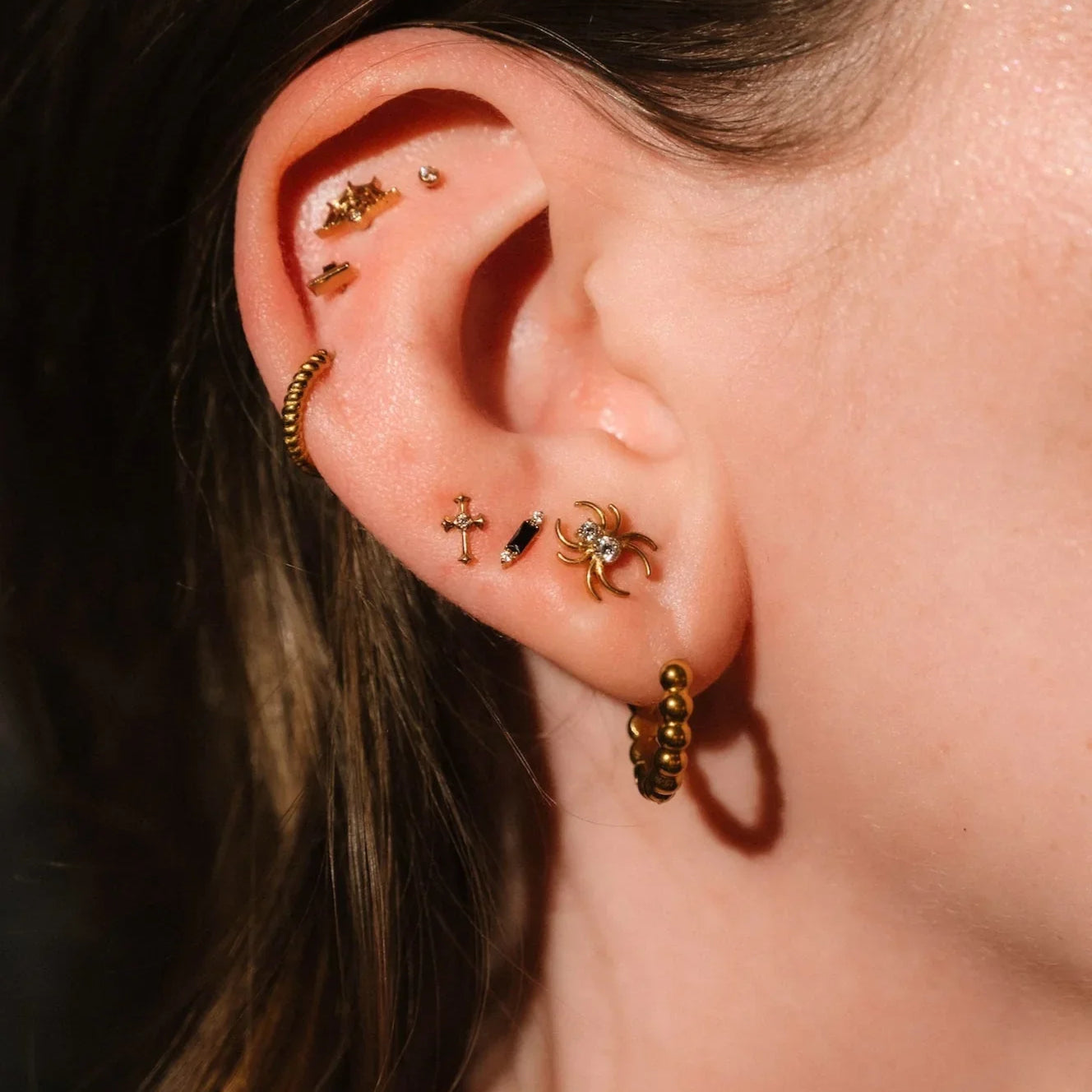 Close up of an ear with black and gold flat backs and hoops