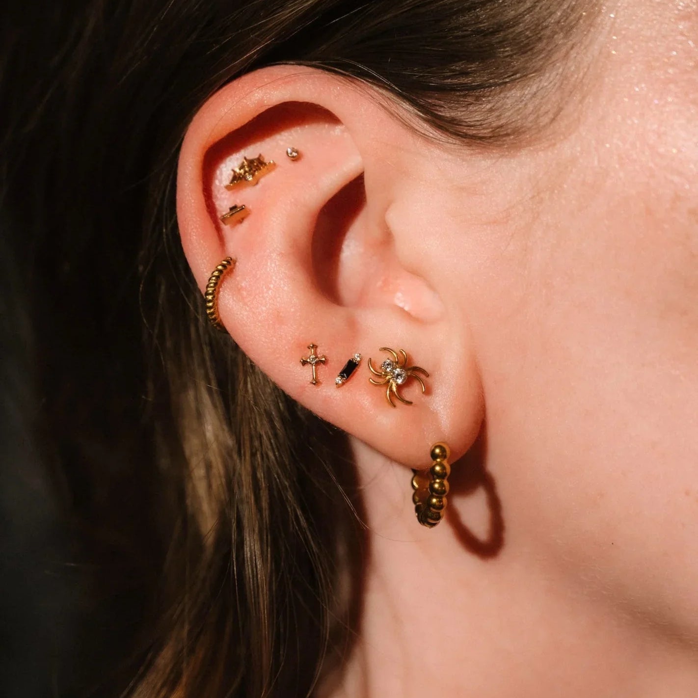 Close up photo of an ear wearing gold and black flat backs