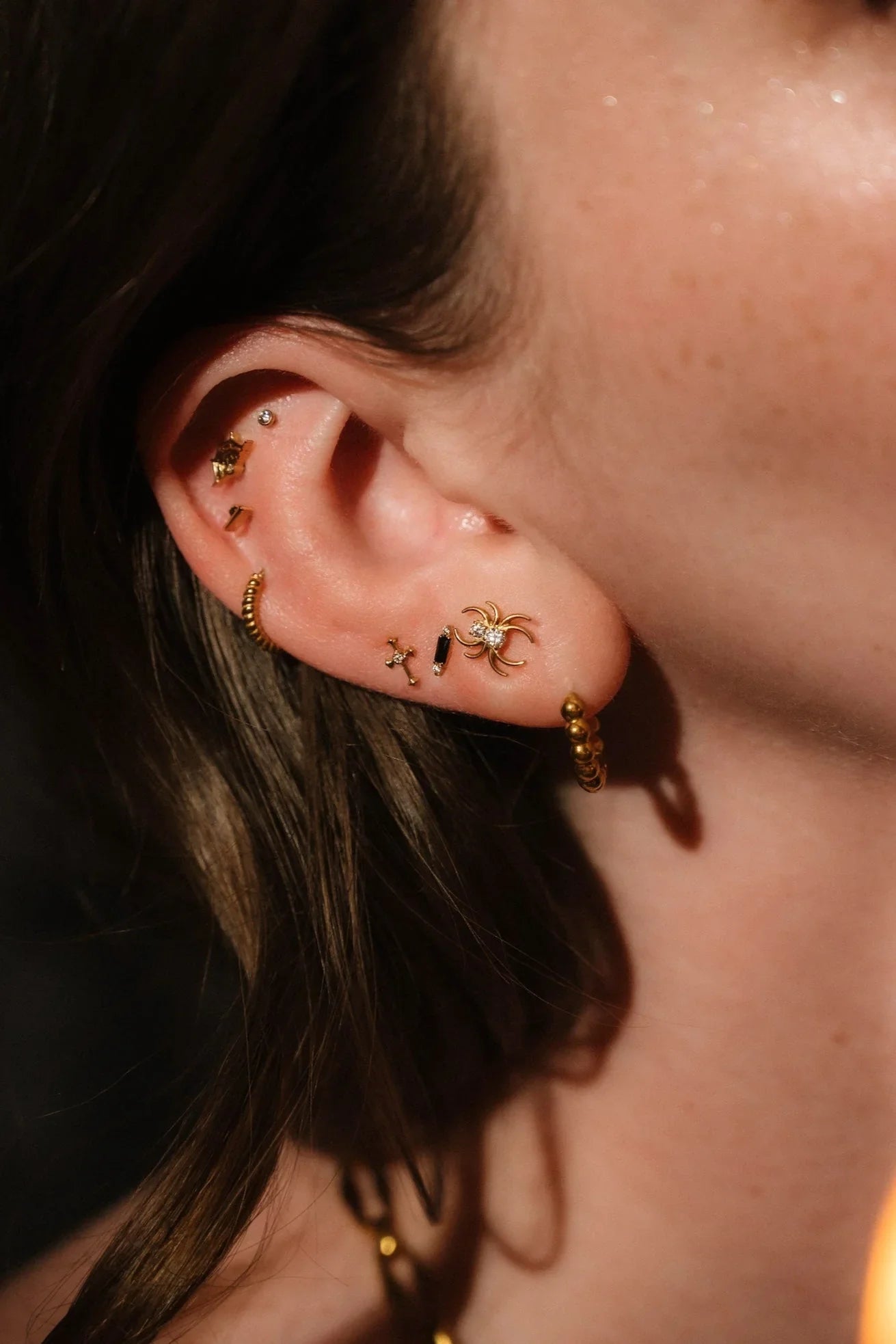 Close up of an ear with black and gold  flat backs and hoops