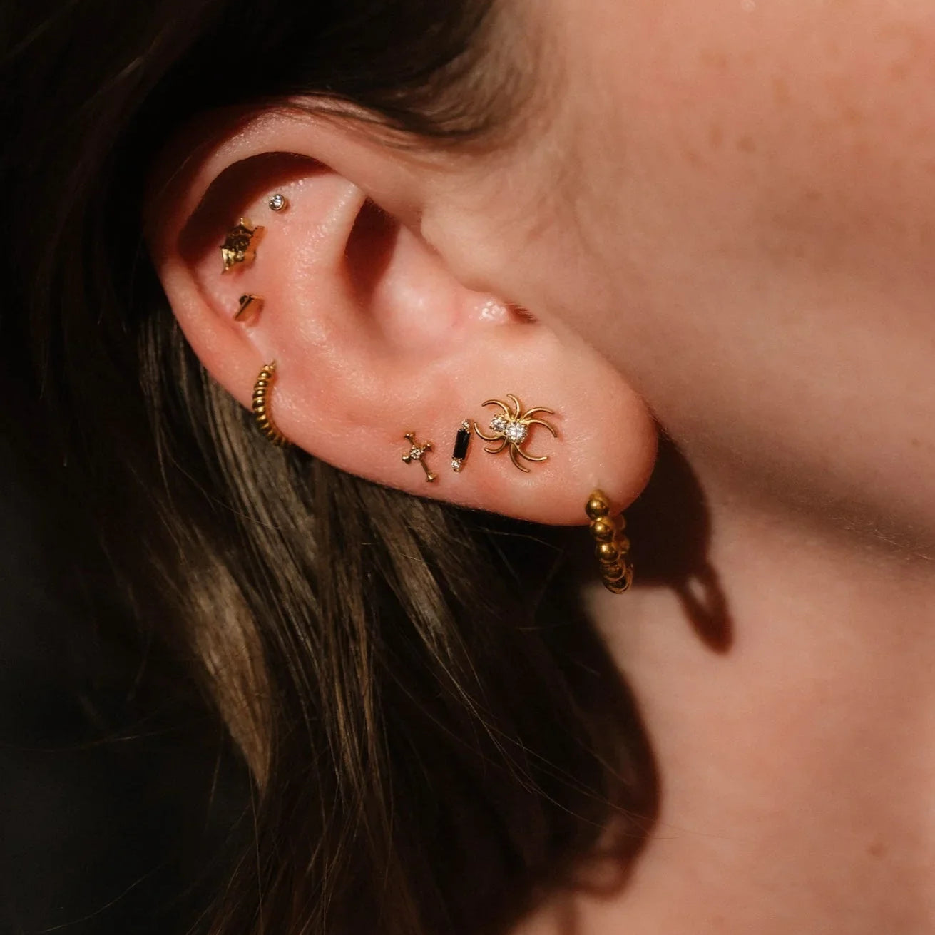 Close up of an ear with black and gold  flat backs and hoops