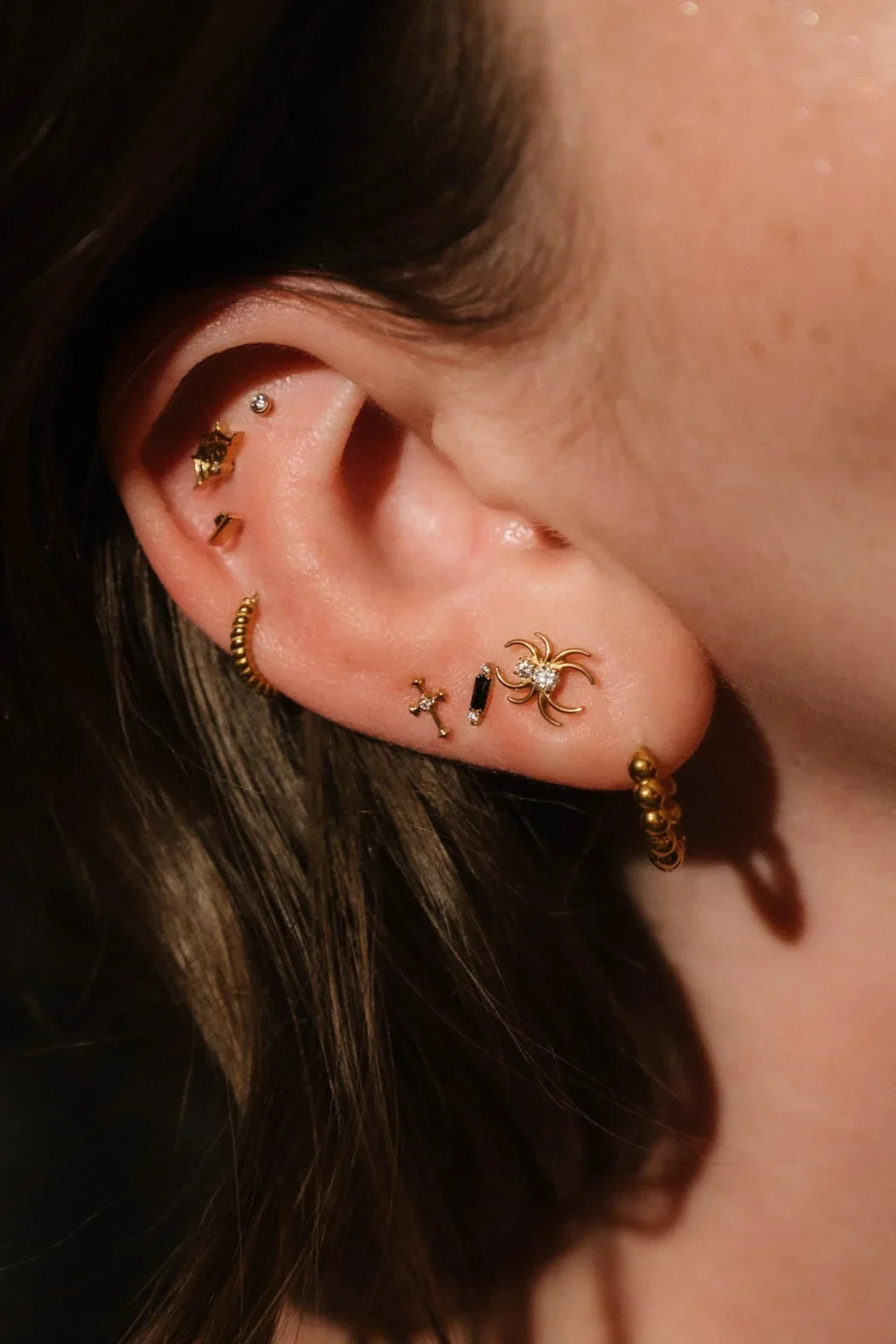 Close up photo of an ear wearing gold and black flat backs