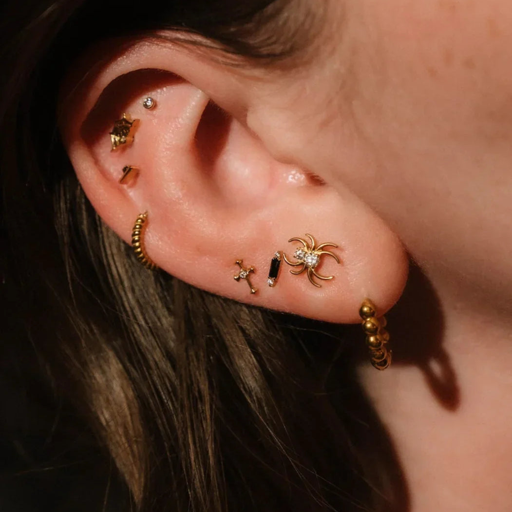 Close up photo of an ear wearing gold and black flat backs