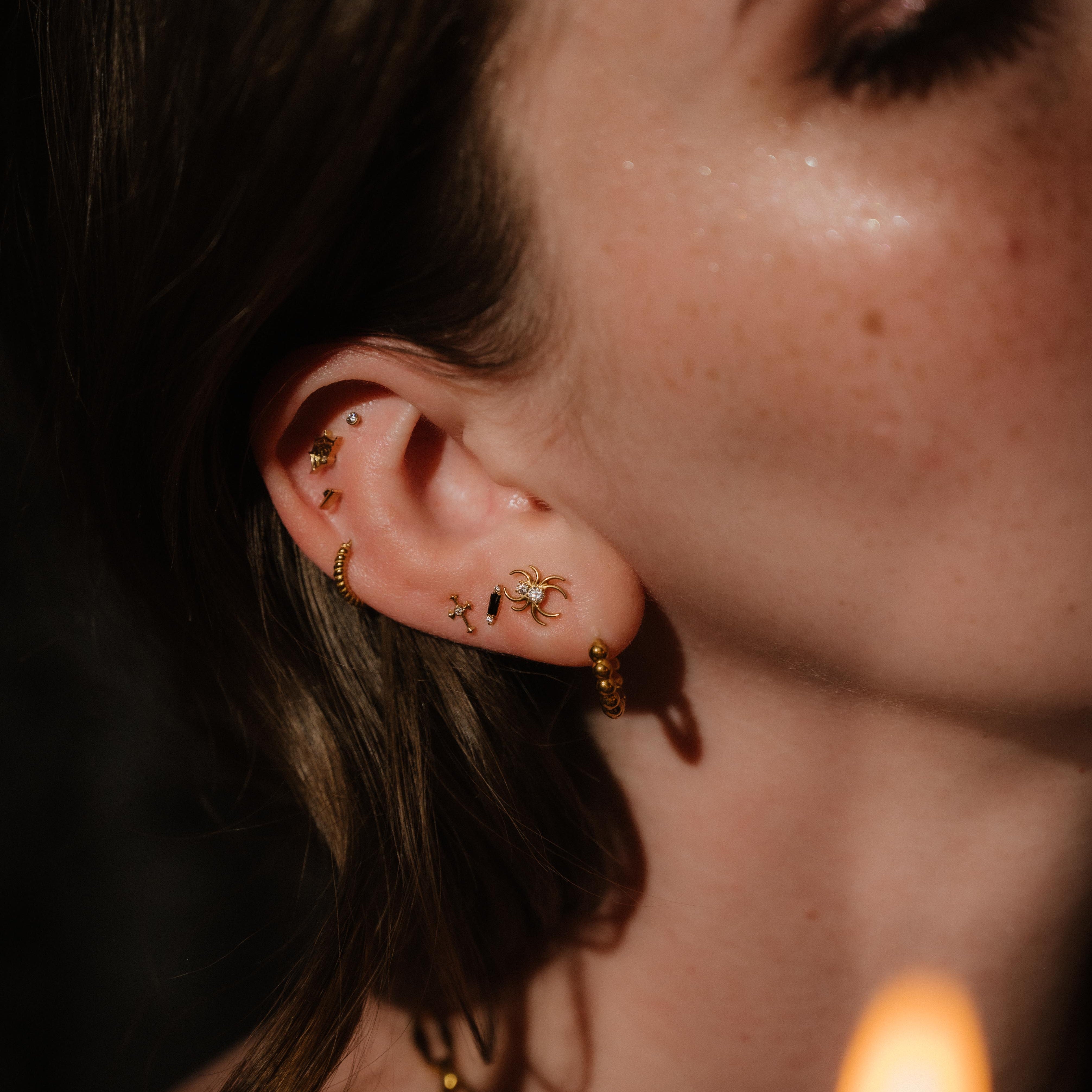 Close-up of a person wearing gold earrings with a blurred candle in the background