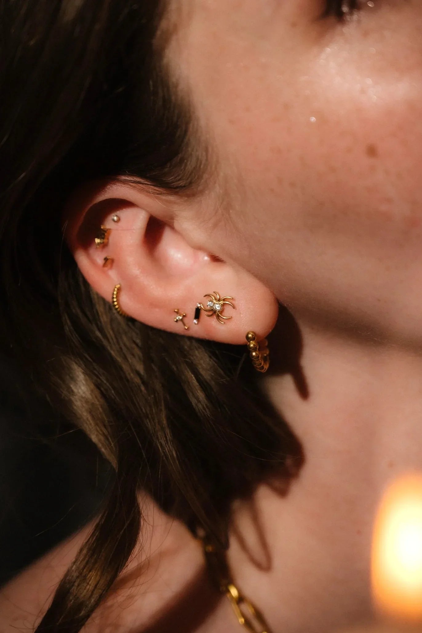 Close-up of an ear with gold earrings against a blurred background