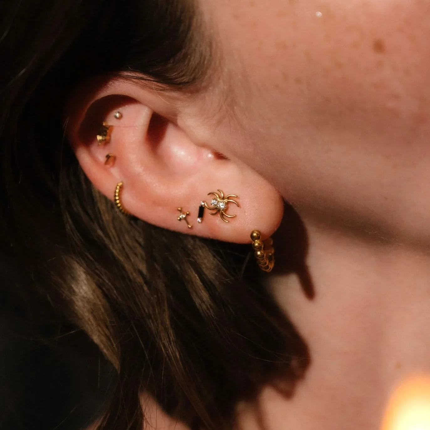 Close-up of an ear with gold earrings against a blurred background