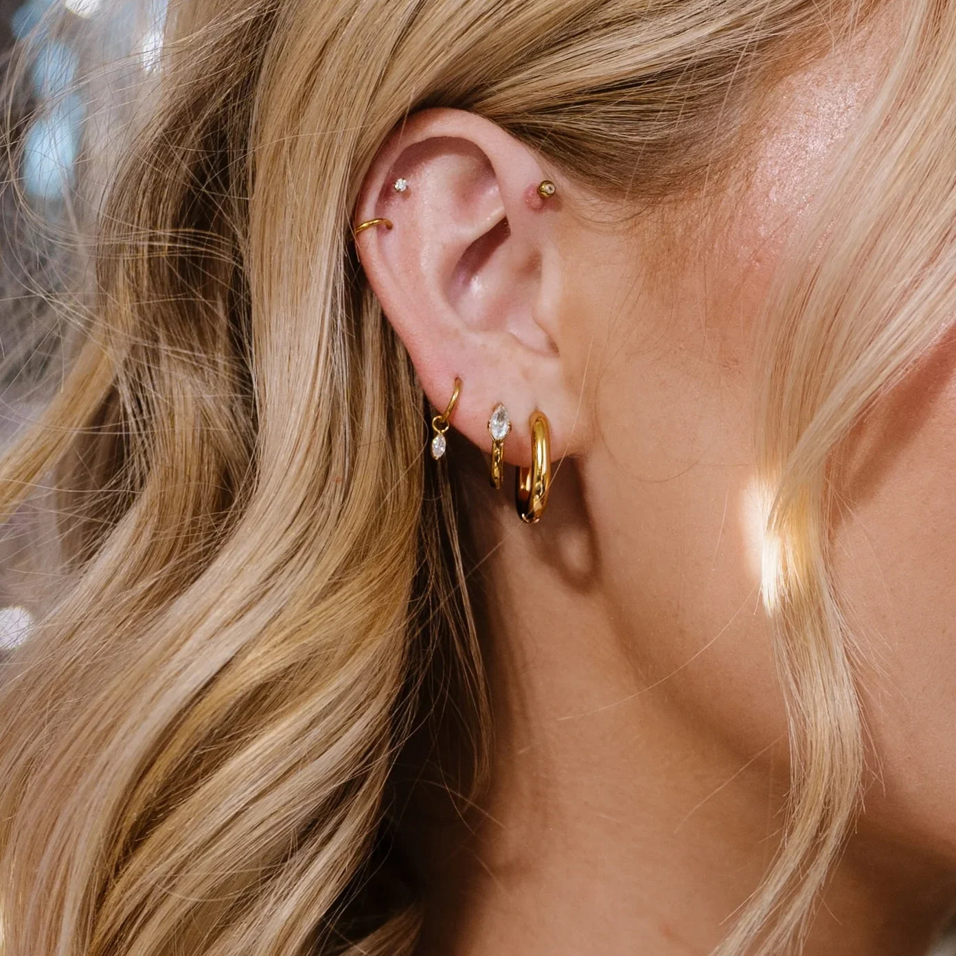 Close-up of an ear with gold hoop earrings and additional jewelry, blurred background