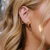 Close-up of an ear with gold hoop earrings and additional jewelry, blurred background