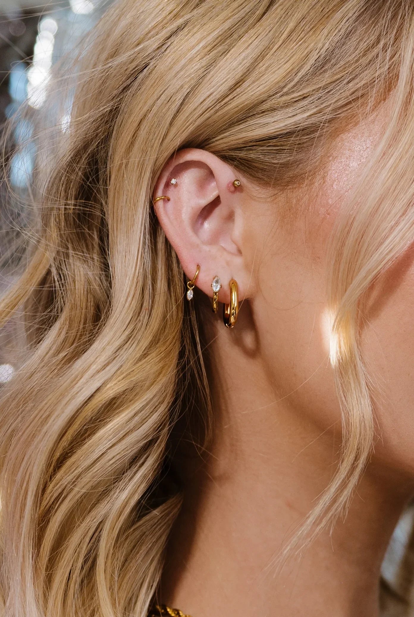 Close-up of an ear with gold hoop earrings and additional jewelry, blurred background