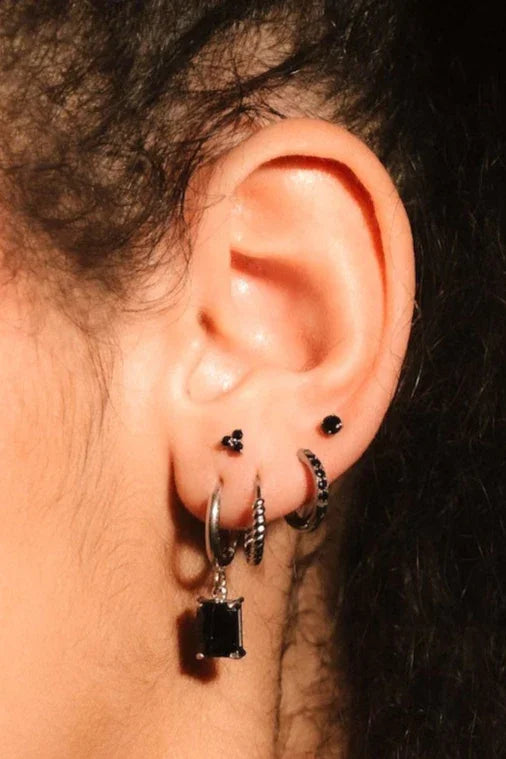 Close up photo of an ear wearing silver and black flat backs and hoops
