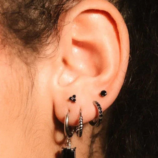 Close up photo of an ear wearing silver and black flat backs and hoops