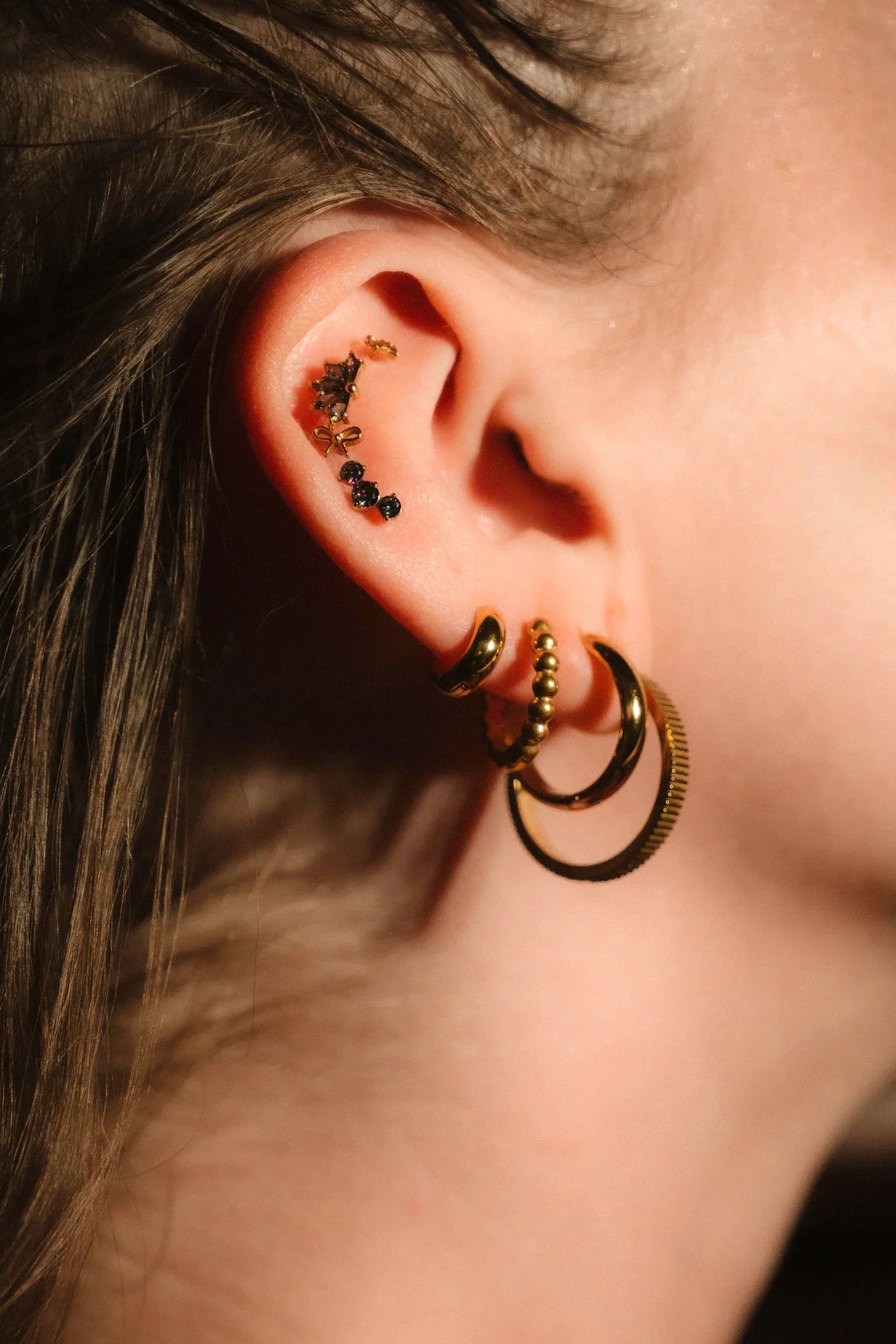 Close-up of an ear with gold hoop earrings and other accessories.