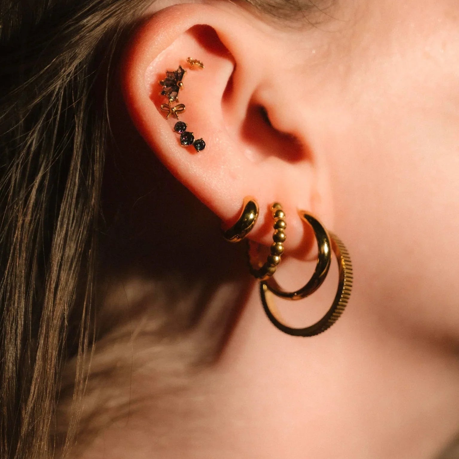 Close-up of an ear with gold hoop earrings and other accessories.