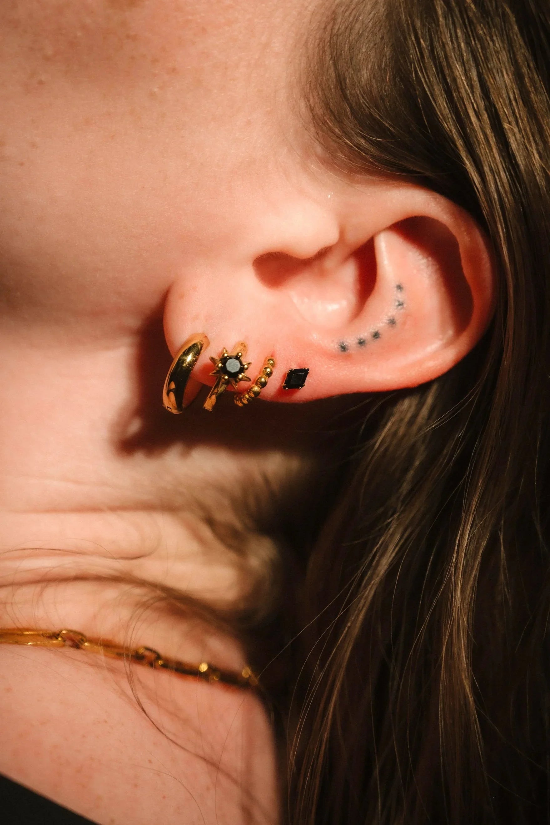 Close up of an ear wearing gold and black flat backs and hoops