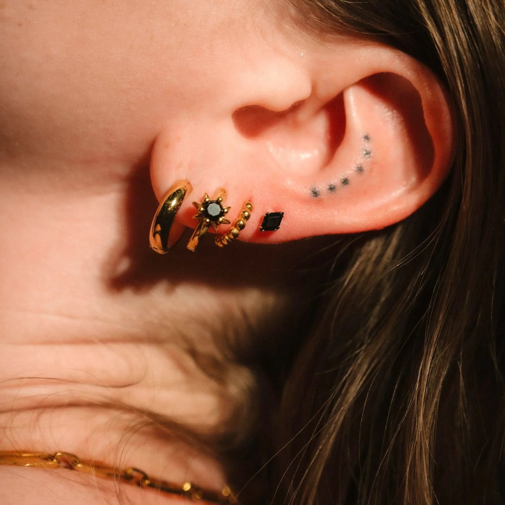 Close up of an ear wearing gold and black flat backs and hoops