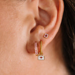 Close-up of an ear wearing gold and enamel hoop earrings with heart designs.