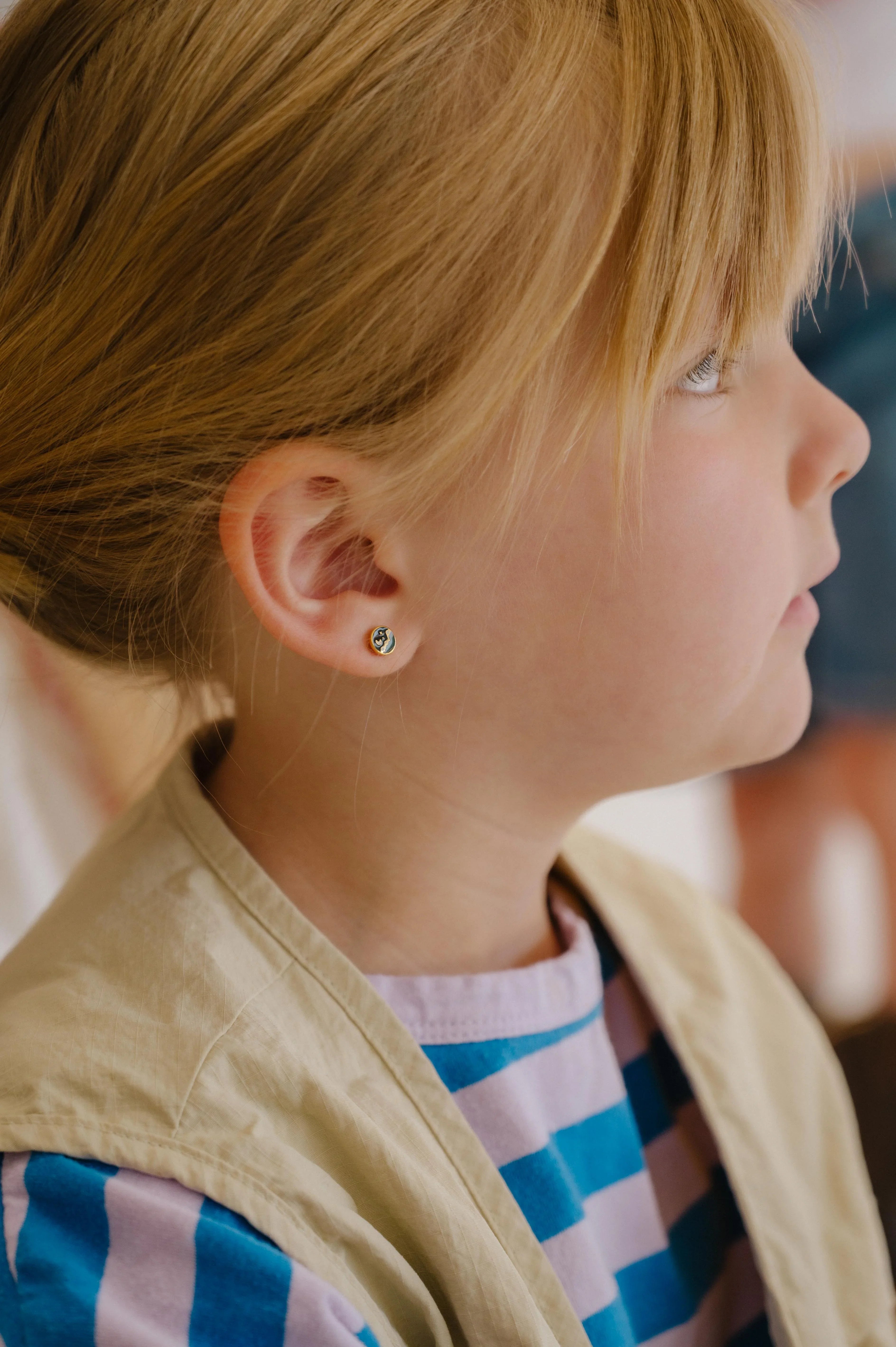 Close-up of child wearing a small circle enamel flat back stud earring that features a tiny night sky scene over a mountain landscape.