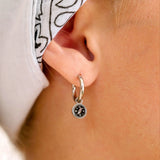 Close-up of an ear wearing a small hoop earring with an enamel compass charm on it.