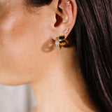 Close-up of an ear wearing multiple gold hoop earrings and flat back studs with a blurred background