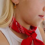 Close-up of a person wearing gold hoop earrings with enamel campfire charm, a red bandana, and a white shirt.