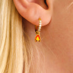 Close-up of a person wearing gold hoop earrings with enamel campfire charm, a red bandana, and a white shirt.