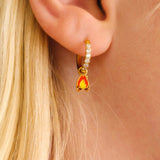 Close-up of a person wearing gold hoop earrings with enamel campfire charm, a red bandana, and a white shirt.