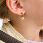 Close-up of a child wearing a colorful striped shirt and beige scarf, with a focus on a hoop earring with an enamel 