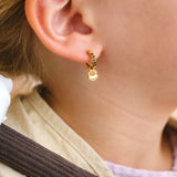 Close-up of a child wearing a colorful striped shirt and beige scarf, with a focus on a hoop earring with an enamel 