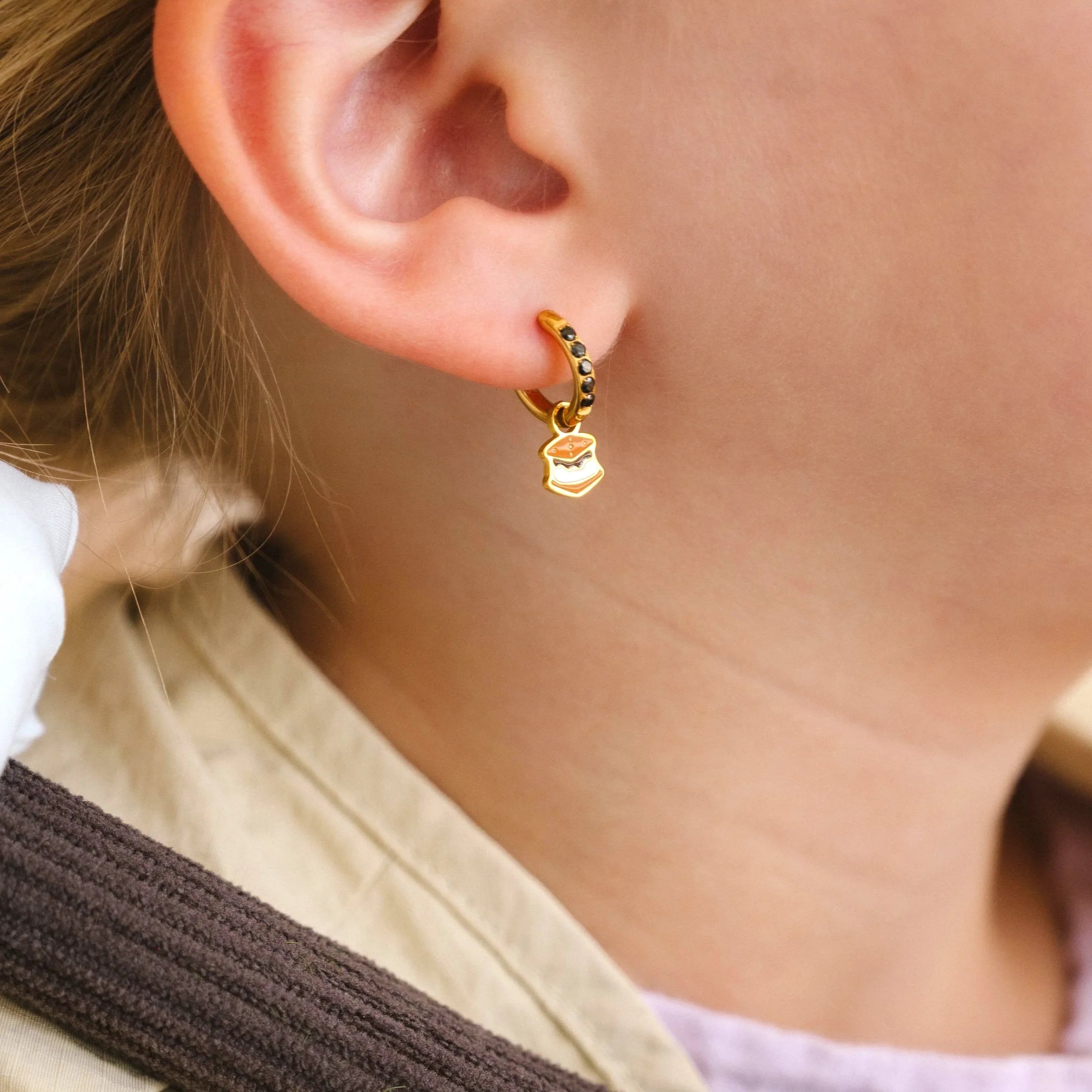 Close-up of a child wearing a colorful striped shirt and beige scarf, with a focus on a hoop earring with an enamel 