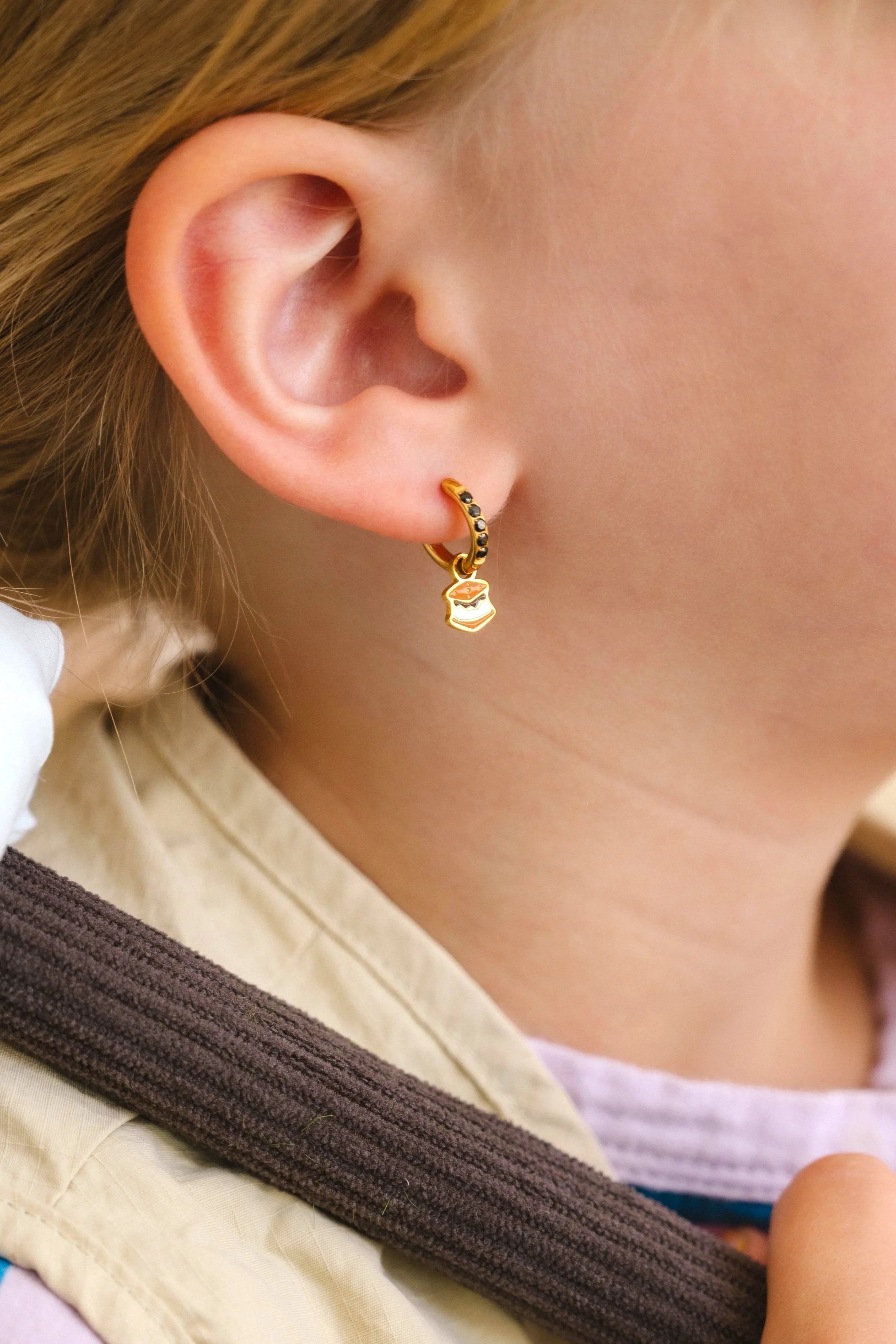 Close-up of a child wearing a colorful striped shirt and beige scarf, with a focus on a hoop earring with an enamel 