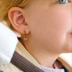 Close-up of a person wearing gold hoop earrings with enamel campfire charm, a red bandana, and a white shirt.