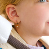 Close-up of a person wearing gold hoop earrings with enamel campfire charm, a red bandana, and a white shirt.