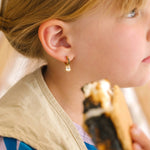 Close-up of a person wearing gold hoop earrings with enamel campfire charm, a red bandana, and a white shirt.