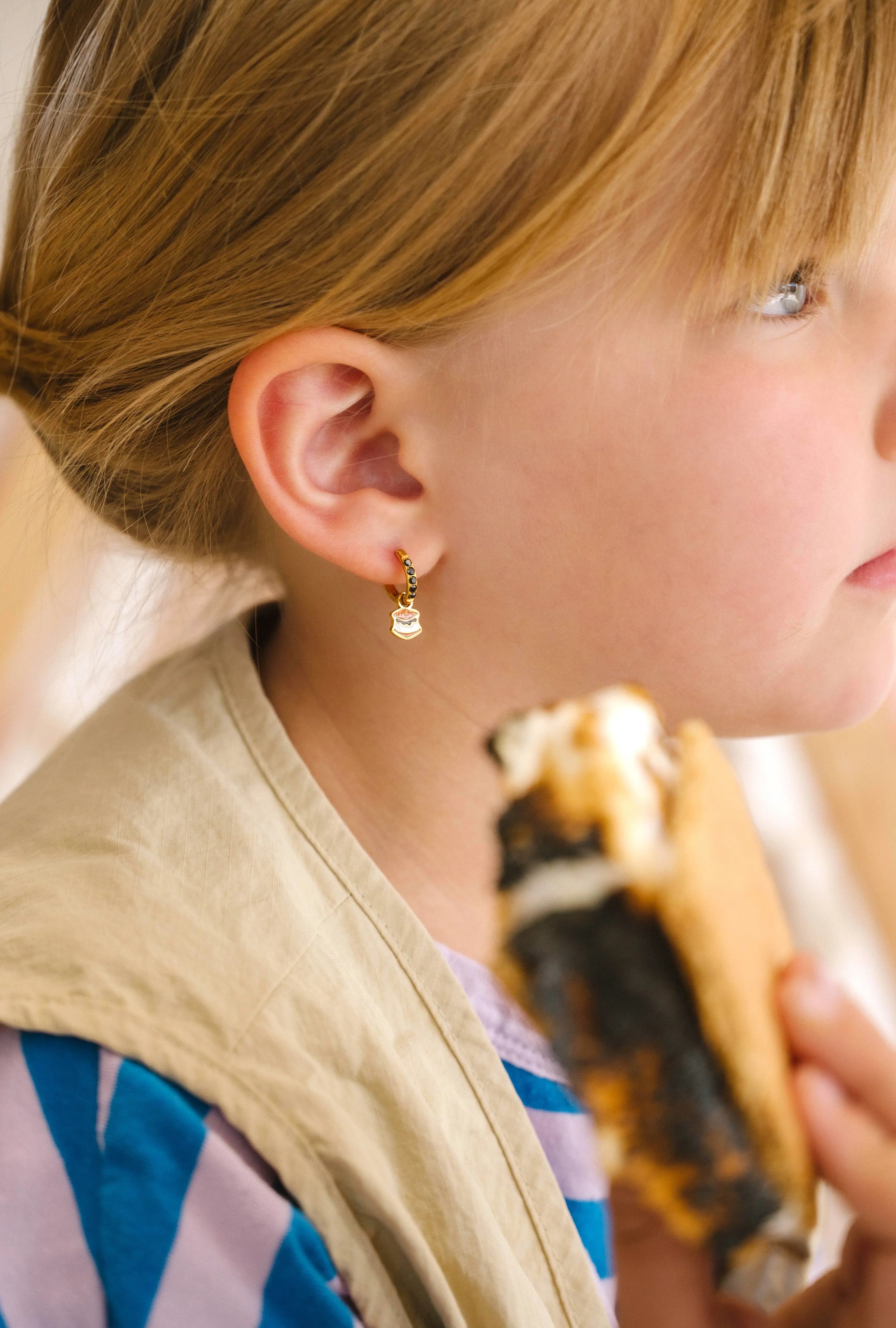 Close-up of a person wearing gold hoop earrings with enamel campfire charm, a red bandana, and a white shirt.