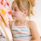 Young child sitting indoors wearing a colorful striped tank top and denim skirt.