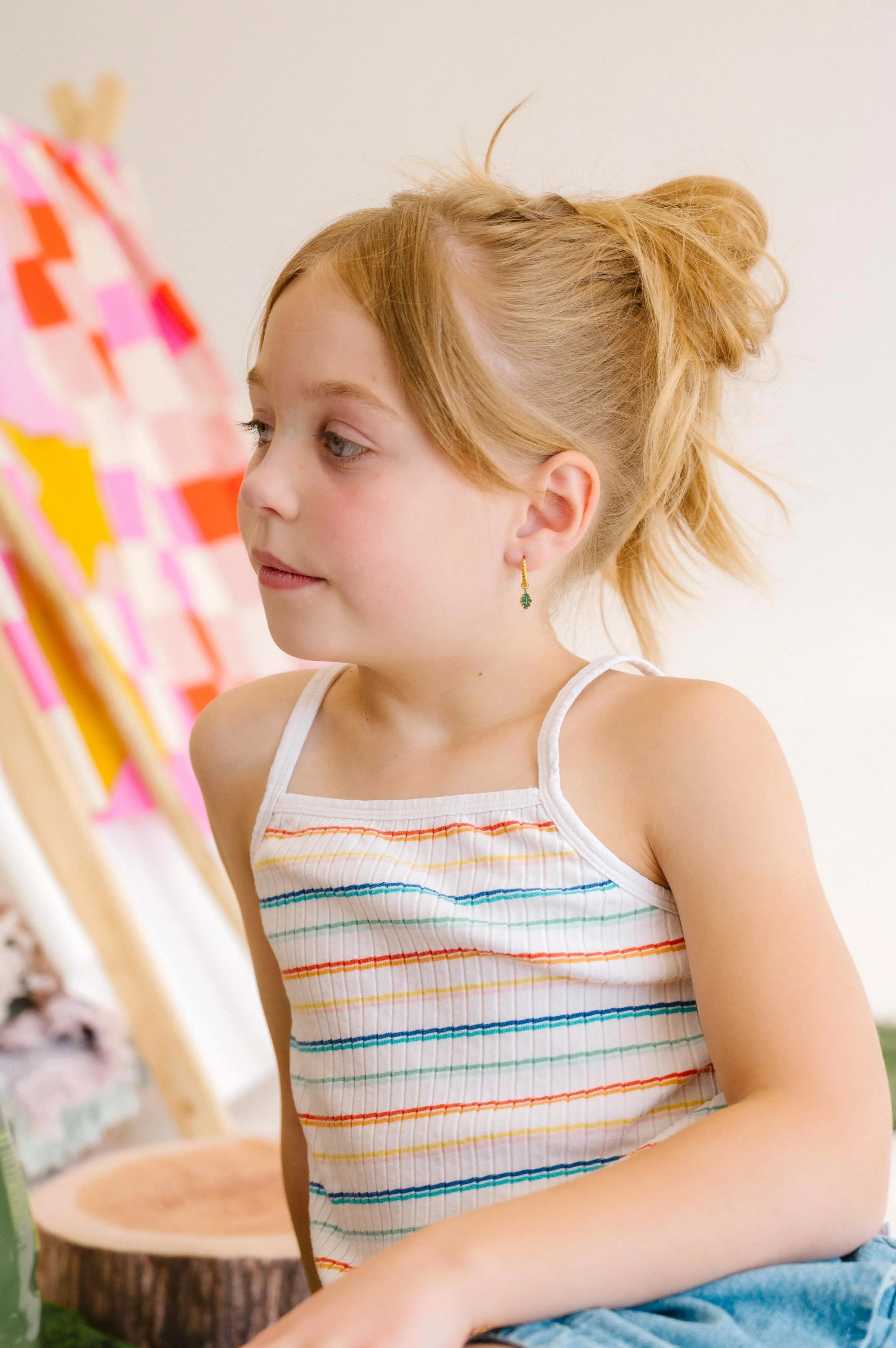Young child sitting indoors wearing a colorful striped tank top and denim skirt.