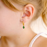 Close-up of a child wearing gold hoop earrings with green and gold oak leaf enamel hoop charm.