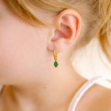 Close-up of a child wearing gold hoop earrings with green and gold oak leaf enamel hoop charm.