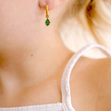 Close-up of a child wearing gold hoop earrings with green and gold oak leaf enamel hoop charm.