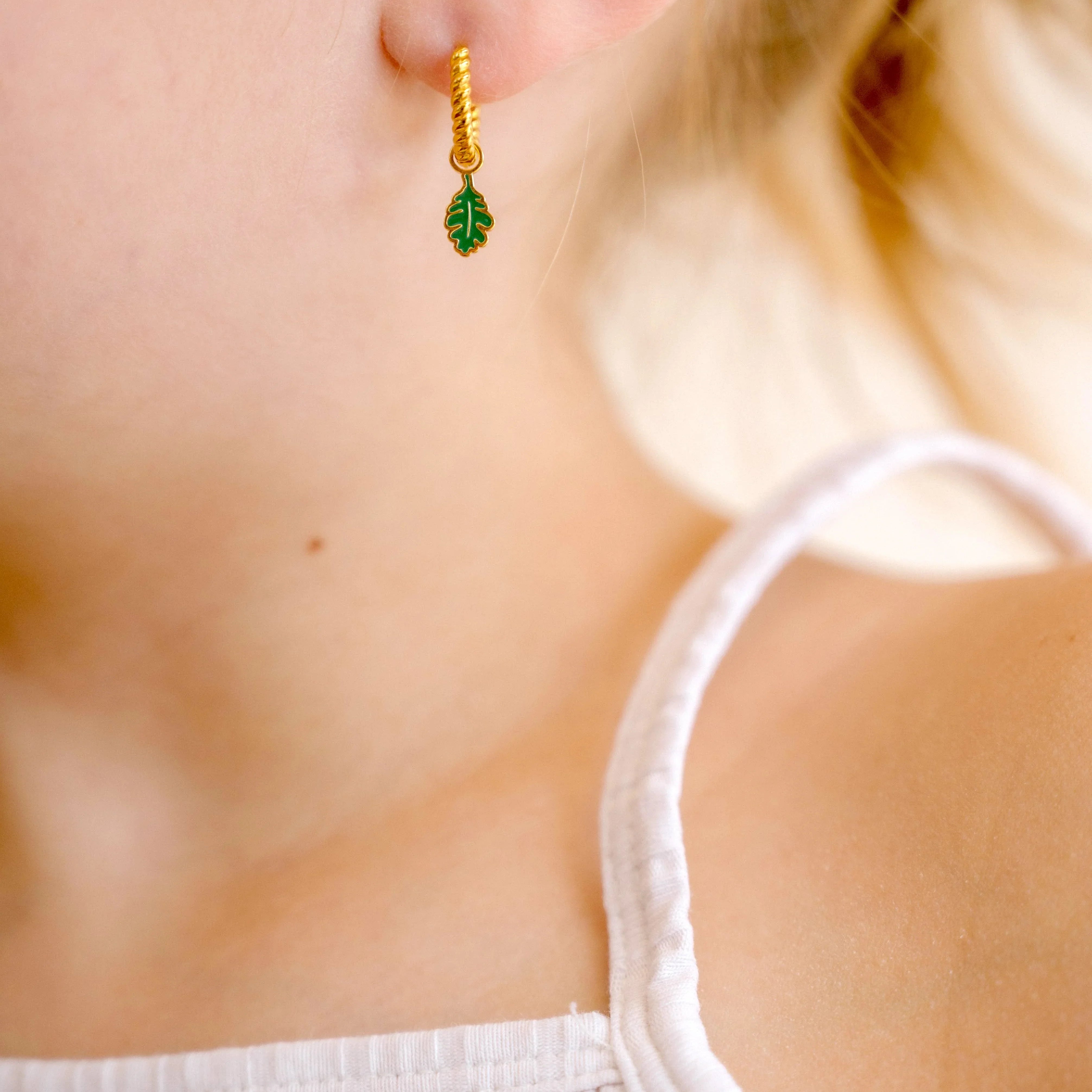 Close-up of a child wearing gold hoop earrings with green and gold oak leaf enamel hoop charm.